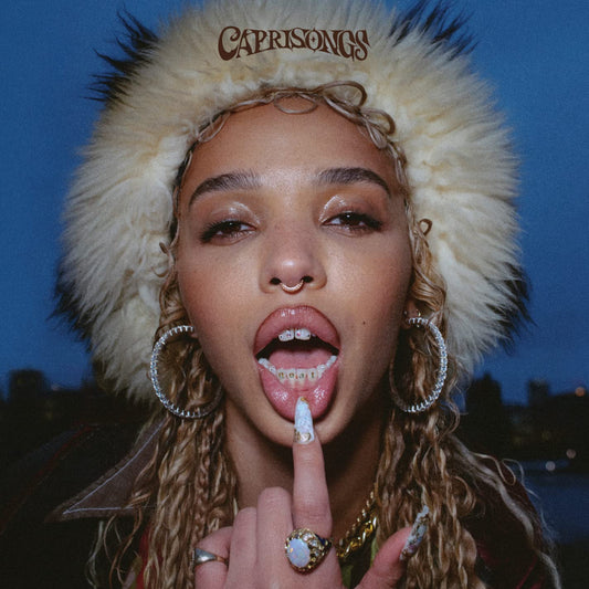FKa twigs wearing a fur hat with 'CAPRISONGS' branding, posing outdoors at night.